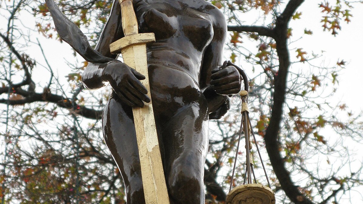 Estatua de la Justicia con espada y balanza entre ramas de árboles