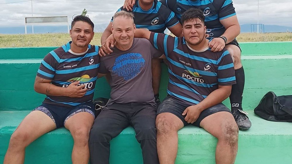 Cinco rugbiers con camisetas a rayas sentados en una tribuna de cemento verde junto a la cancha