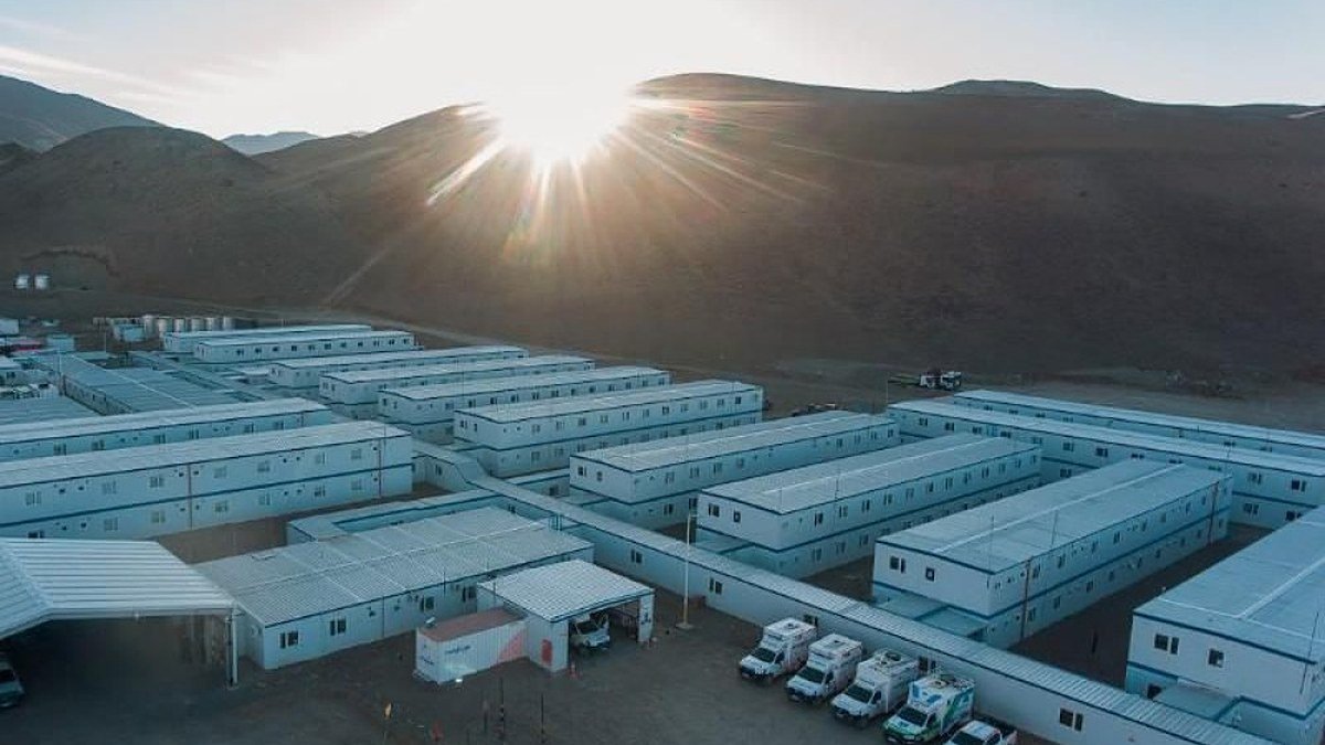 Campamento de módulos blancos del proyecto minero Josemaría al pie de cerros, con el sol de frente