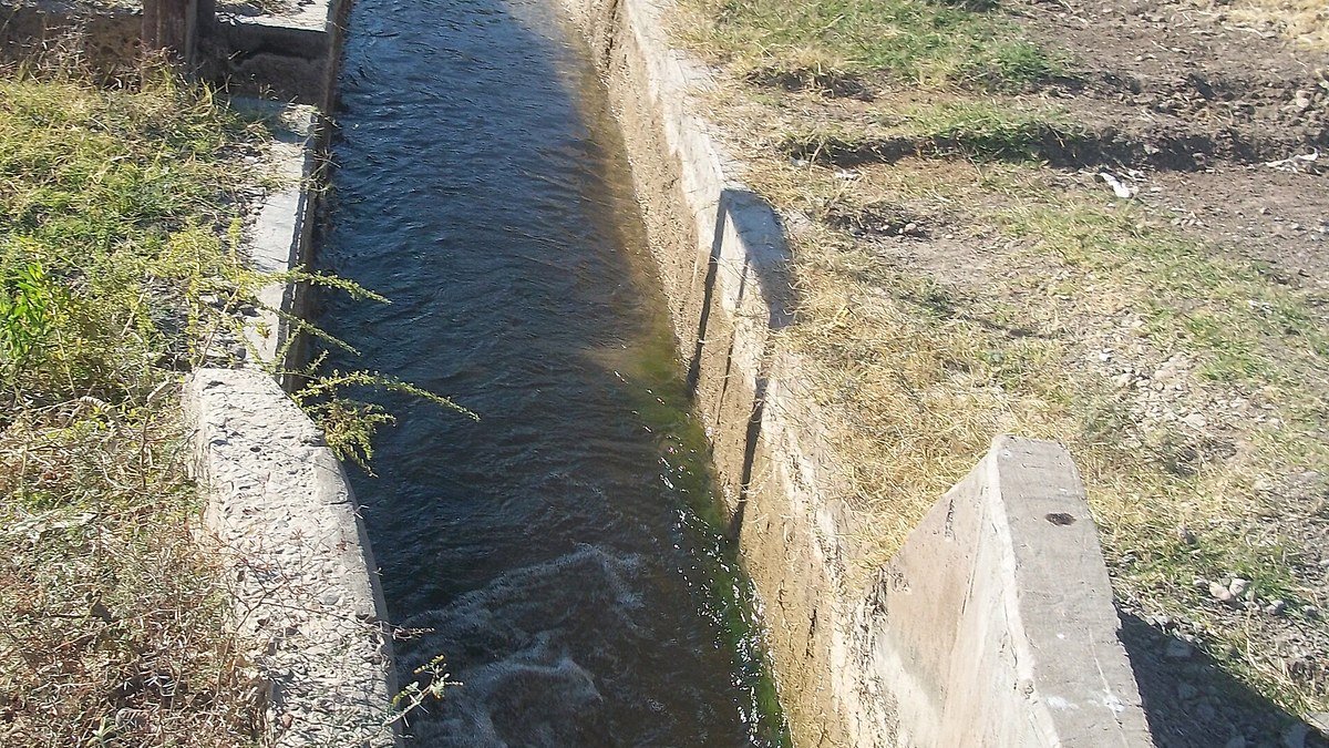 Canal de riego de hormigón con agua, entre pastizales, en Tres Esquinas, Sarmiento