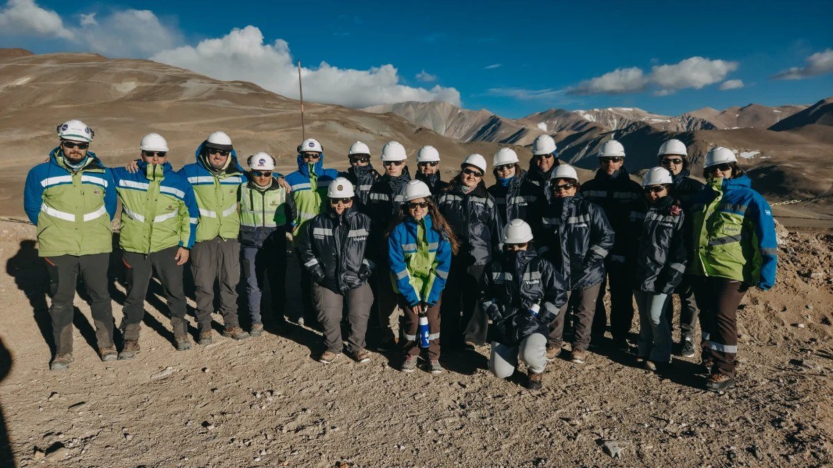 Un grupo de personas con cascos y ropa de trabajo posa en un sector de montaña del proyecto Vicuña