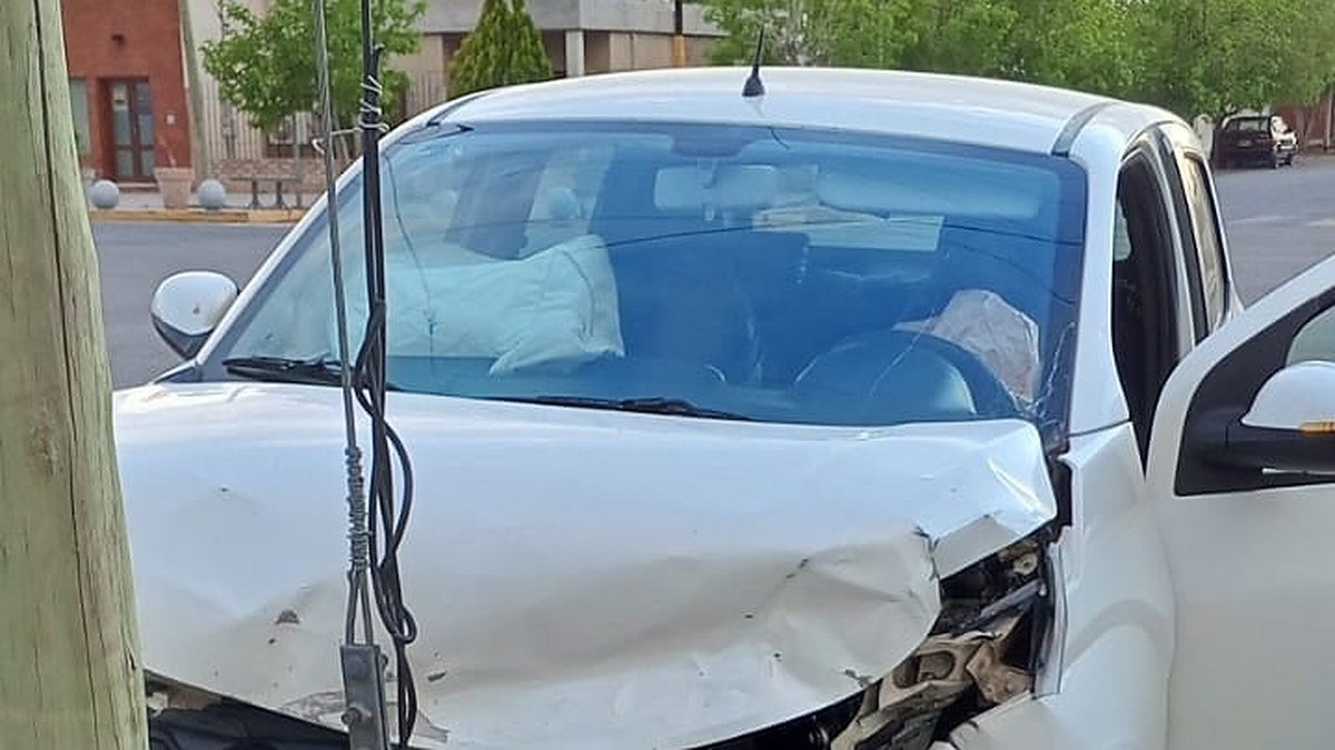 Auto blanco con el frente destrozado y las bolsas de aire desplegadas, junto a un poste de madera en una vereda de Media Agua