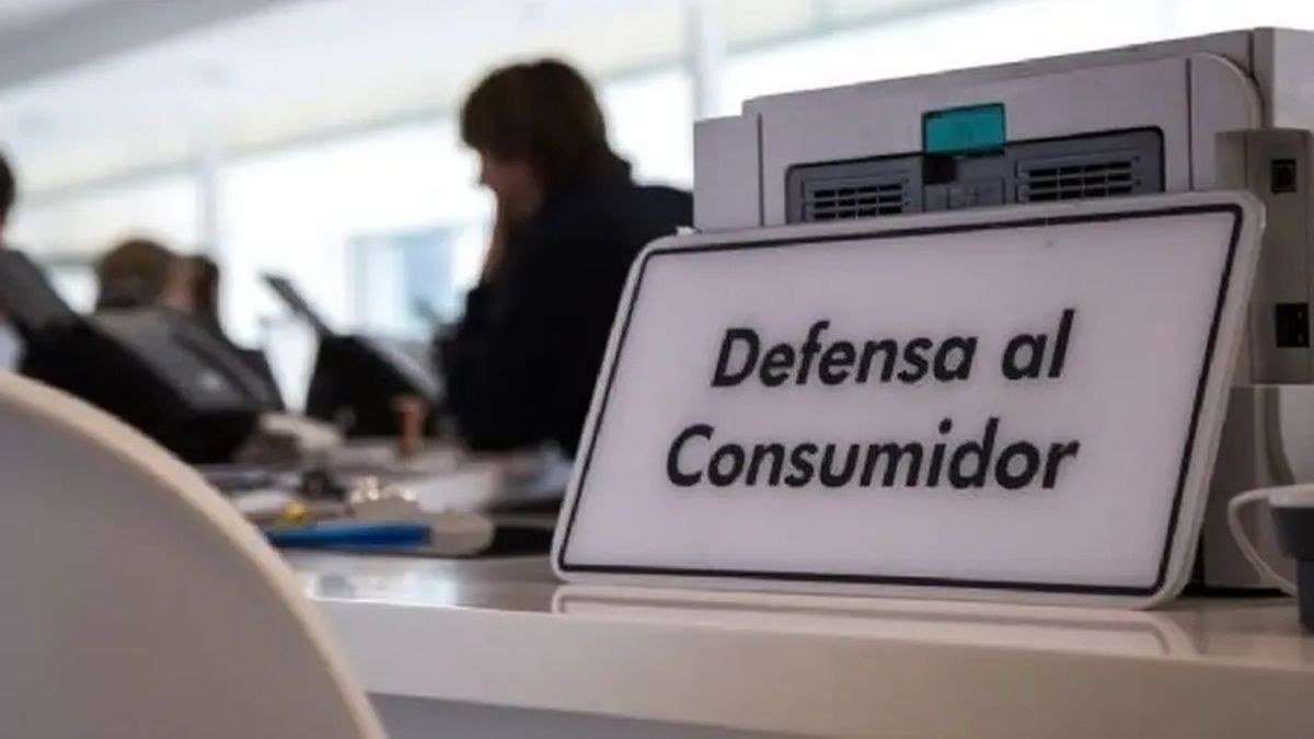 Cartel de Defensa al Consumidor sobre un mostrador de atención, con empleados desenfocados al fondo