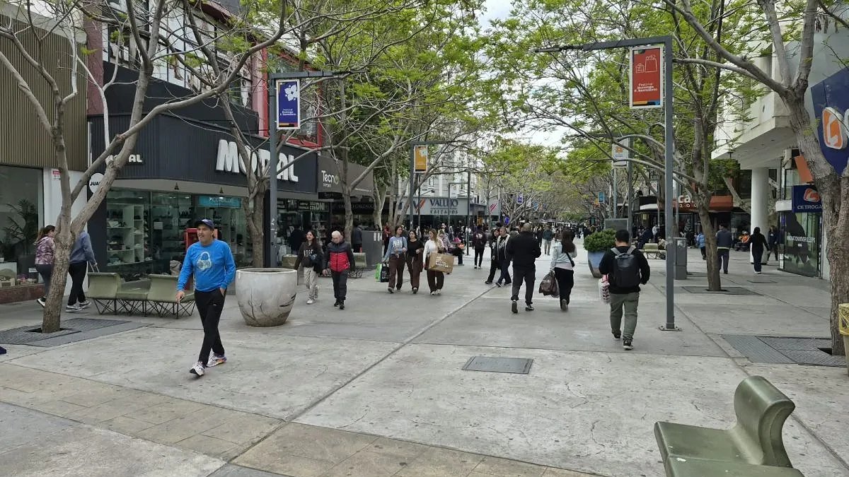 Peatones con bolsas de compras caminan por la peatonal arbolada del centro de San Juan