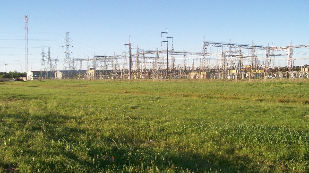 Estación transformadora eléctrica con torres y estructuras metálicas detrás de un campo de césped