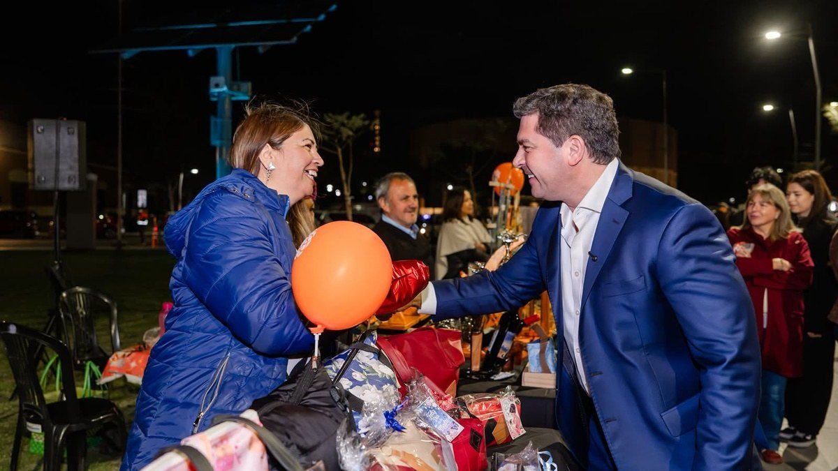 El gobernador Marcelo Orrego saluda a una emprendedora en un puesto de la Expo Mamá, de noche, en el Parque Belgrano