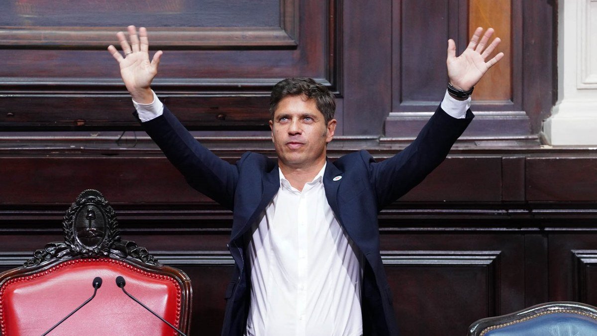 Axel Kicillof, de saco oscuro y camisa blanca, levanta los brazos en el recinto de la Legislatura bonaerense