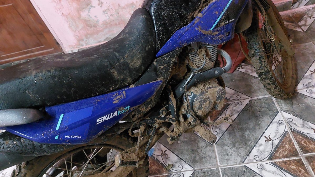 Moto Motomel azul cubierta de barro, estacionada en el interior de una vivienda