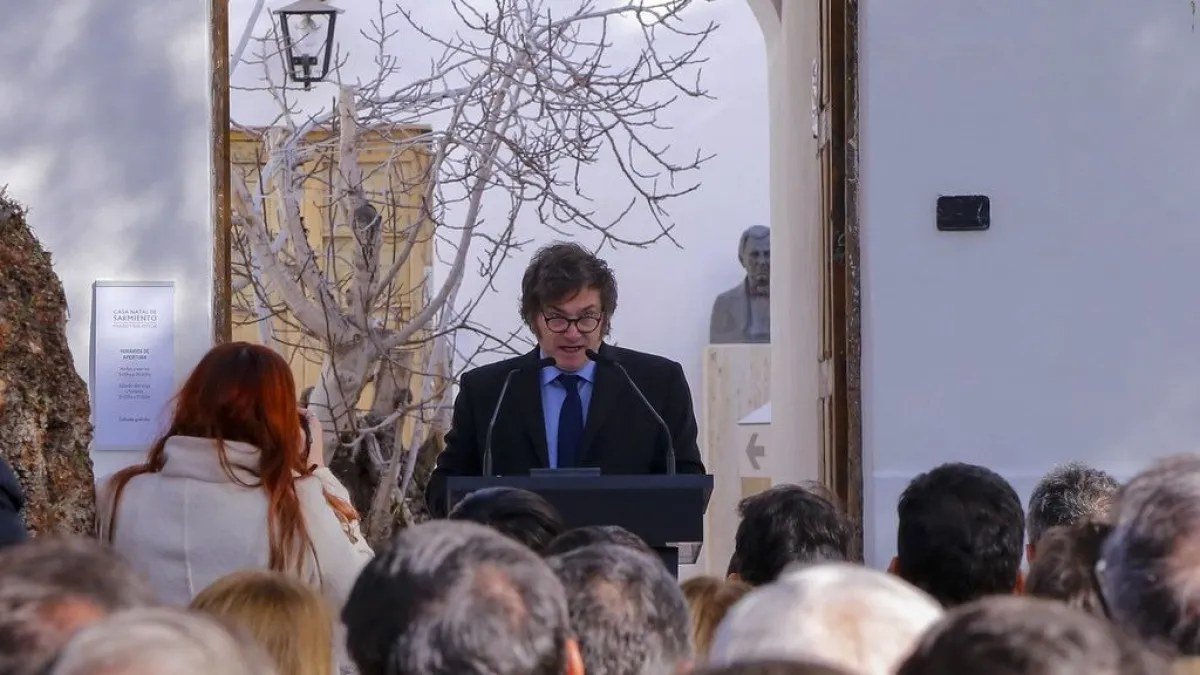 Javier Milei habla en un atril frente al público, en un patio con un árbol sin hojas