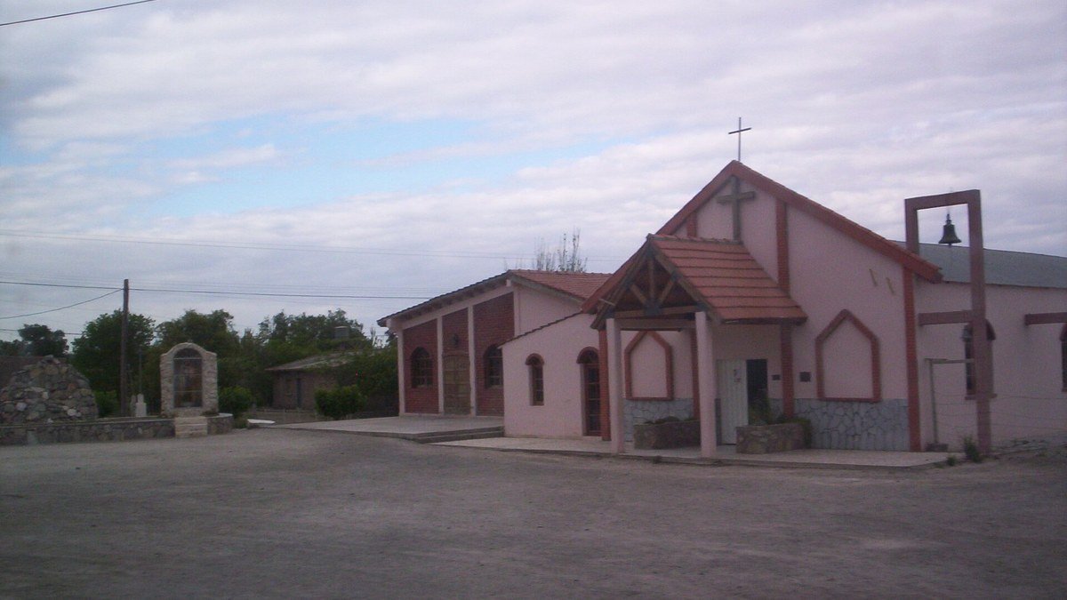 Iglesia de Los Berros, de paredes rosadas y techo de tejas, con un campanario lateral bajo un cielo nublado