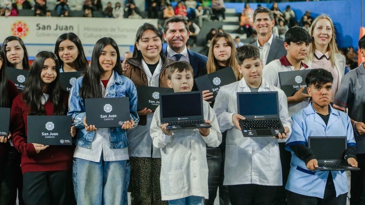 Estudiantes de guardapolvo muestran sus computadoras nuevas junto al gobernador Marcelo Orrego en un estadio