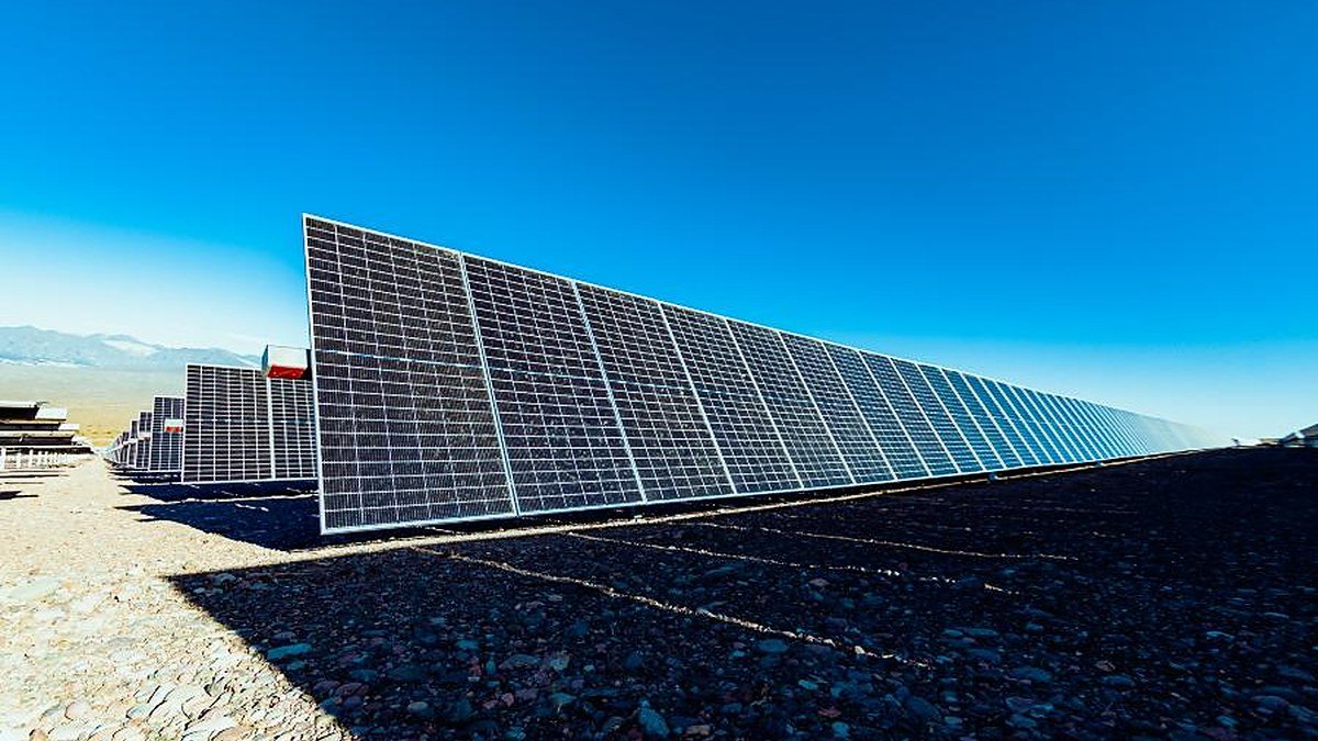 Hilera de paneles solares sobre suelo pedregoso bajo un cielo azul en un parque solar de San Juan