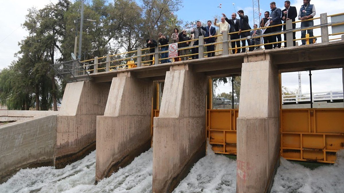 Autoridades provinciales sobre la pasarela del Partidor San Emiliano mientras el agua sale por las compuertas