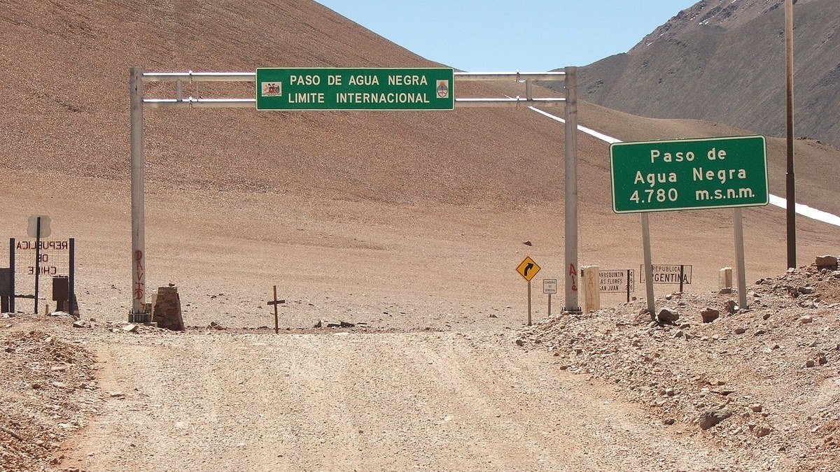 Pórtico verde del límite internacional y cartel de altura de 4.780 metros en el Paso de Agua Negra, sobre un camino de ripio