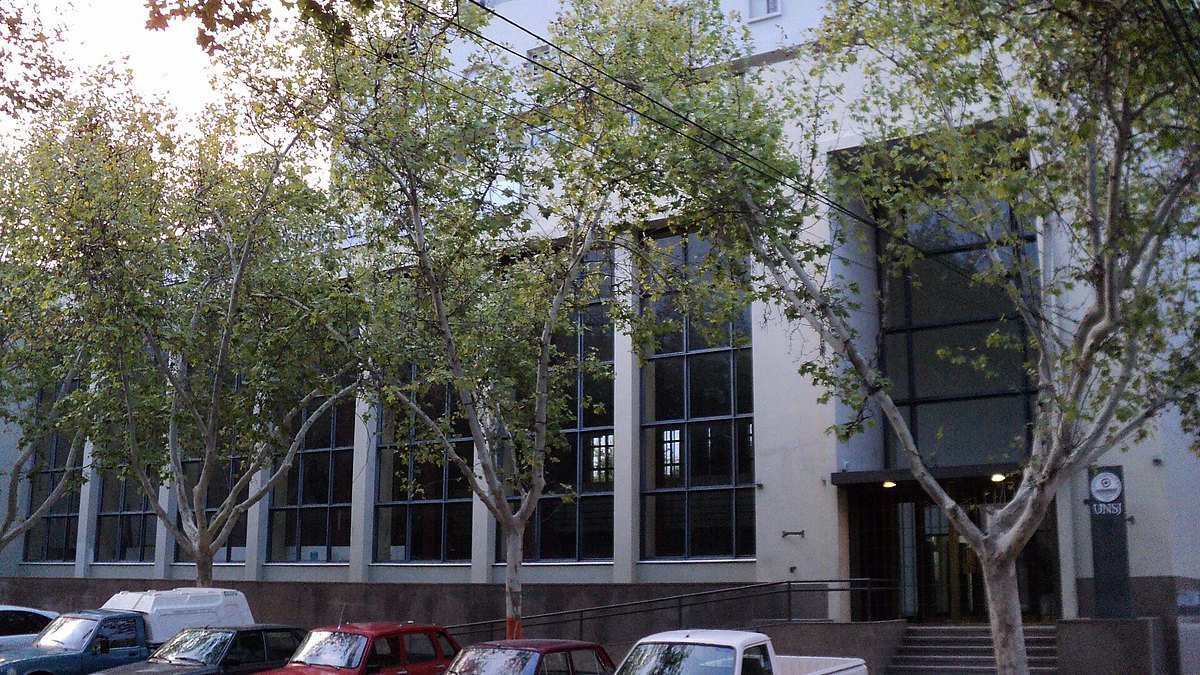 Fachada del edificio del Rectorado de la Universidad Nacional de San Juan, con árboles y autos estacionados