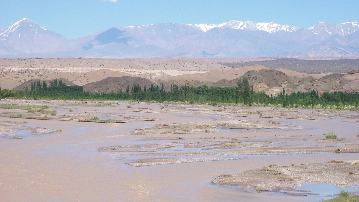 Cauce ancho y barroso del río San Juan cerca de Calingasta, con la cordillera nevada al fondo