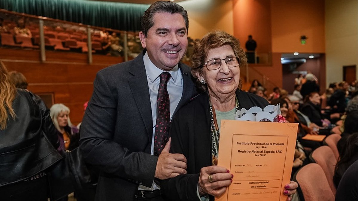 El gobernador Marcelo Orrego posa junto a una mujer que muestra la carpeta de su escritura del IPV, en un auditorio con público