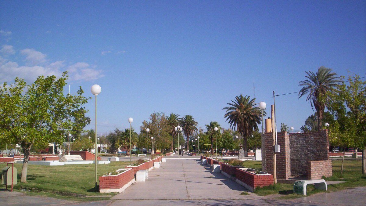Plaza de Villa Media Agua, en Sarmiento, con palmeras, faroles y canteros de ladrillo bajo un cielo despejado