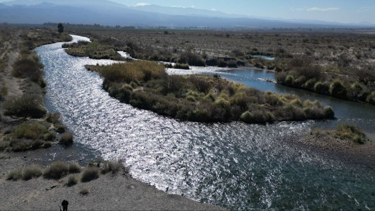 Río de aguas claras que serpentea entre la vegetación baja y la costa pedregosa