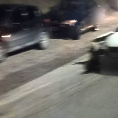 Auto blanco con el frente dañado sobre la Ruta 153, de noche, con otros vehículos y un camión con luces encendidas detrás
