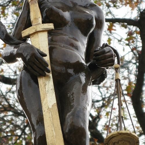 Estatua de la Justicia con espada y balanza entre ramas de árboles