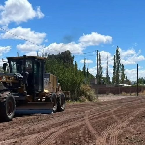 Motoniveladora trabajando sobre una calle de tierra en Barreal, con álamos y cielo con nubes