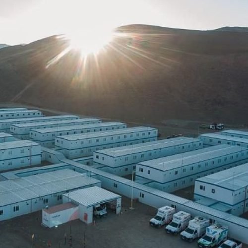 Campamento de módulos blancos del proyecto minero Josemaría al pie de cerros, con el sol de frente