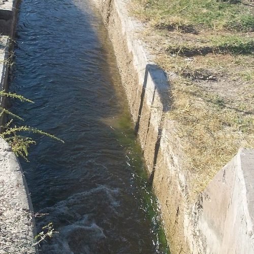 Canal de riego de hormigón con agua, entre pastizales, en Tres Esquinas, Sarmiento