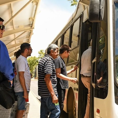 Pasajeros suben a un colectivo blanco en una parada techada de la ciudad de San Juan