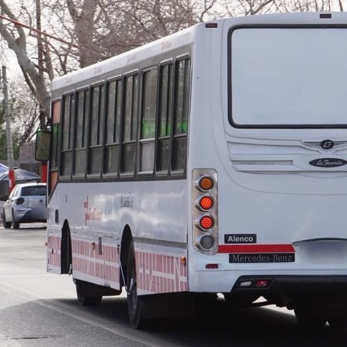 Colectivo blanco de pasajeros circulando por una calle de San Juan, visto desde atrás