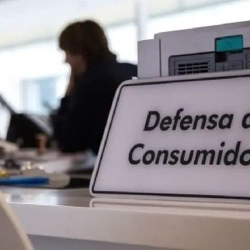 Cartel de Defensa al Consumidor sobre un mostrador de atención, con empleados desenfocados al fondo