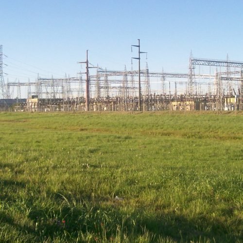 Estación transformadora eléctrica con torres y estructuras metálicas detrás de un campo de césped