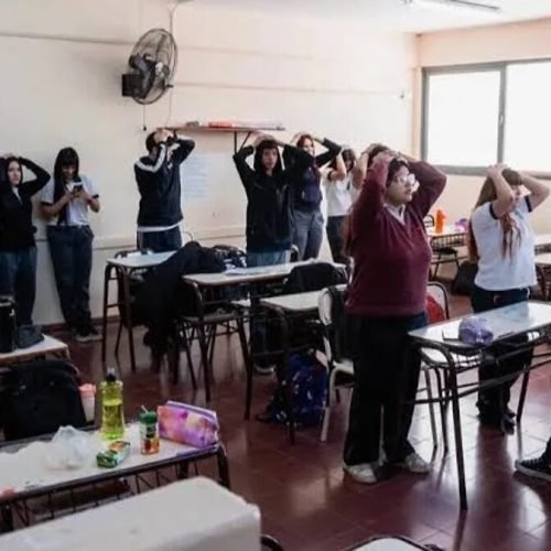Estudiantes en aula durante un simulacro de sismo, con las manos sobre la cabeza
