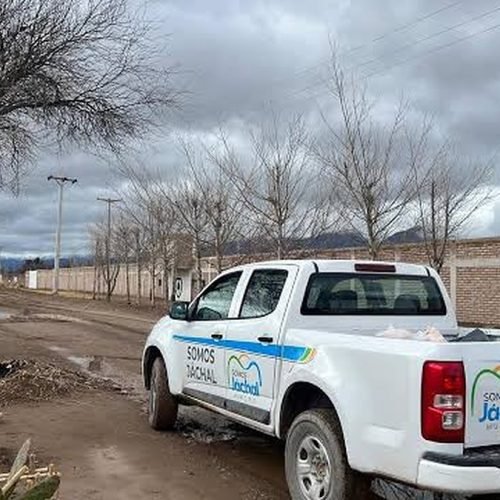 Camioneta blanca del Municipio de Jáchal estacionada en una calle de tierra embarrada, con cielo nublado