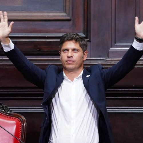 Axel Kicillof, de saco oscuro y camisa blanca, levanta los brazos en el recinto de la Legislatura bonaerense