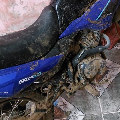 Moto Motomel azul cubierta de barro, estacionada en el interior de una vivienda
