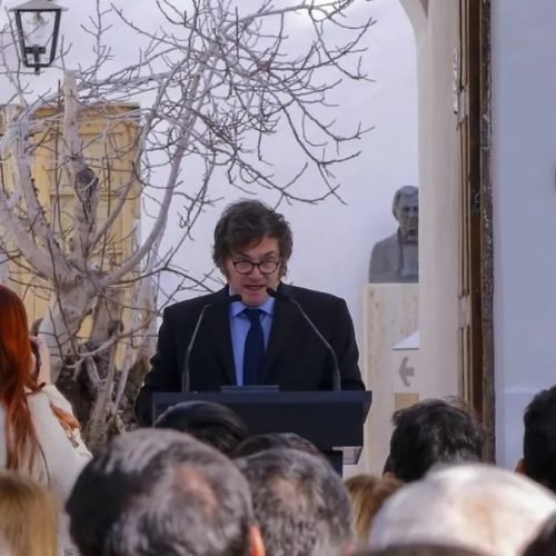 Javier Milei habla en un atril frente al público, en un patio con un árbol sin hojas