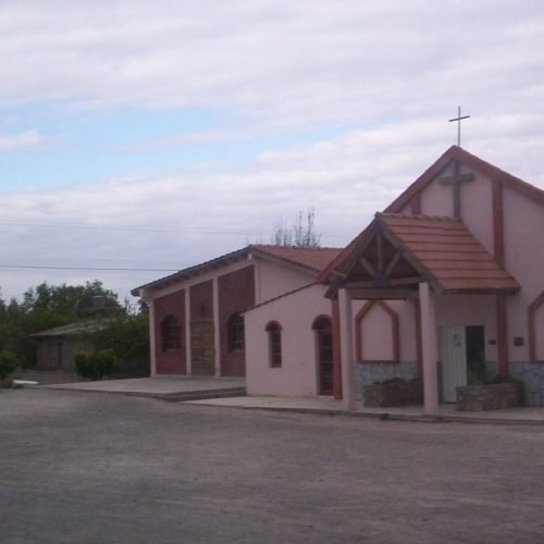 Iglesia de Los Berros, de paredes rosadas y techo de tejas, con un campanario lateral bajo un cielo nublado