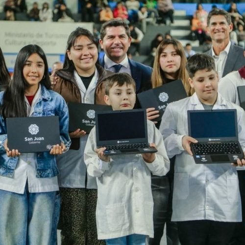 Estudiantes de guardapolvo muestran sus computadoras nuevas junto al gobernador Marcelo Orrego en un estadio