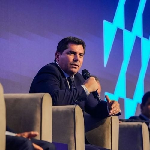 Marcelo Orrego habla con un micrófono, sentado en un panel frente a una pantalla azul