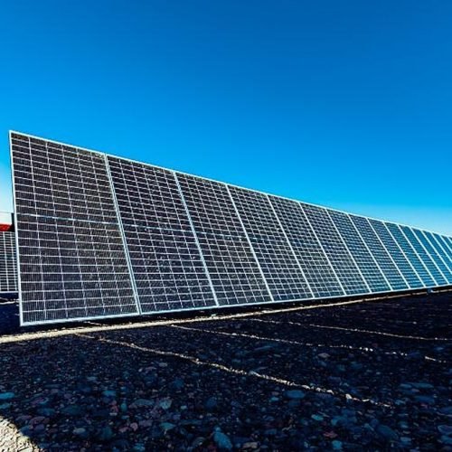 Hilera de paneles solares sobre suelo pedregoso bajo un cielo azul en un parque solar de San Juan