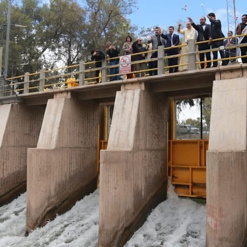 Autoridades provinciales sobre la pasarela del Partidor San Emiliano mientras el agua sale por las compuertas