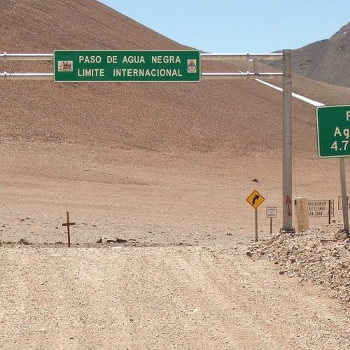 Pórtico verde del límite internacional y cartel de altura de 4.780 metros en el Paso de Agua Negra, sobre un camino de ripio