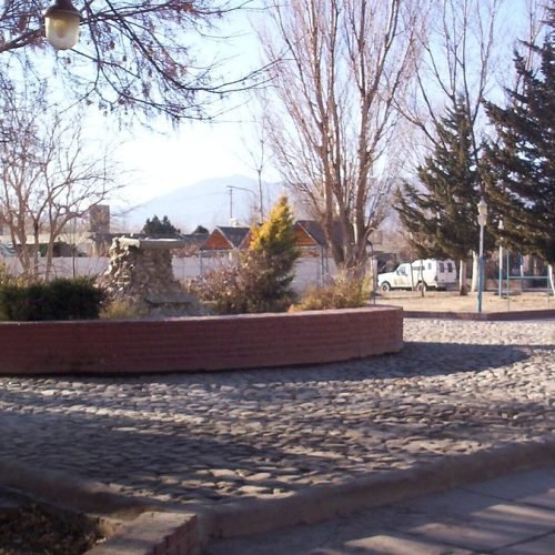 Plaza de Rodeo, en Iglesia, con árboles sin hojas, faroles y montañas al fondo