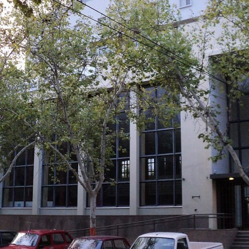 Fachada del edificio del Rectorado de la Universidad Nacional de San Juan, con árboles y autos estacionados