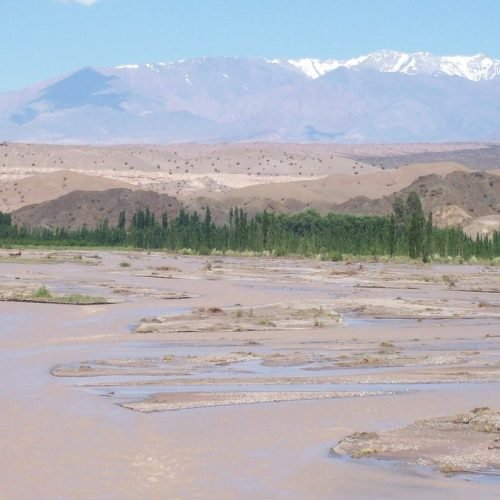 Cauce ancho y barroso del río San Juan cerca de Calingasta, con la cordillera nevada al fondo