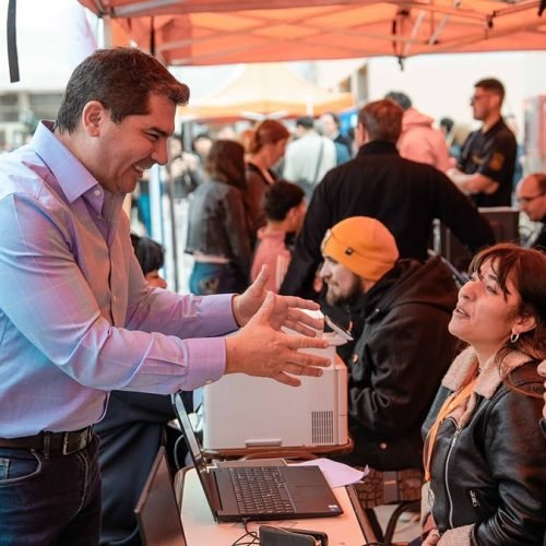 Marcelo Orrego conversa con vecinas sentadas frente a un puesto de atención bajo un gazebo