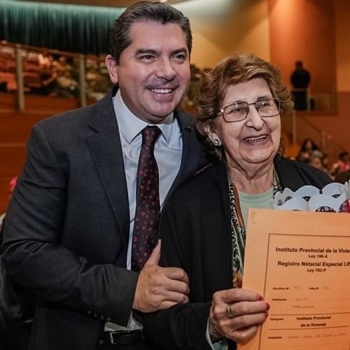 El gobernador Marcelo Orrego posa junto a una mujer que muestra la carpeta de su escritura del IPV, en un auditorio con público