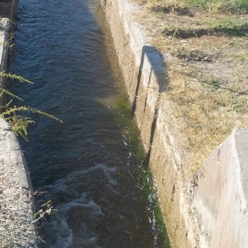 Canal de riego de hormigón con agua en una zona rural de Tres Esquinas, Sarmiento