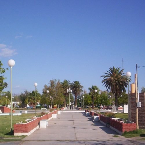 Plaza de Villa Media Agua, en Sarmiento, con palmeras, faroles y canteros de ladrillo bajo un cielo despejado